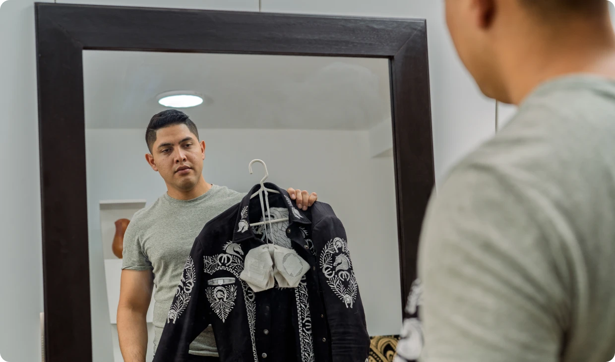 Man holding mariachi suit in front of mirror.